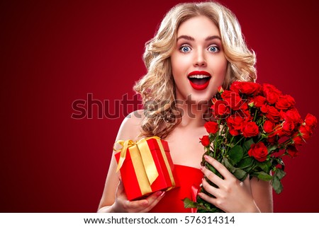 Beautiful blonde woman holding bouquet of red roses and gift. Saint Valentine and International Women's Day, Eight March celebration.