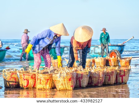 Binh Thuan, Vietnam - January 21st, 2016: Two fishermen stoop anchovies carrying baskets expressed strenuous labor in bringing fish sauce processing at fishing village in Binh Thuan, Vietnam