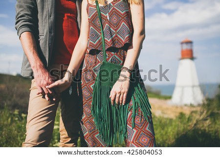 man and woman holding hands, hipster style, vintage 70's outfit, boho, indie trend, printed overall, green suede bag with fringe, lighthouse on background, nature, summer, stylish accessories