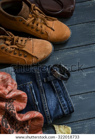 women's autumn clothing and accessories - boots, jeans, scarf, bag, on dark wood surfaces, vintage style