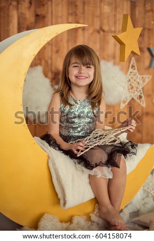 Happy baby girl 5-6 year old sitting on a wooden month with a decorative star in her hands. Children's photozone. Childhood.