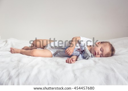 Sleeping baby in his crib, holding a teddy bear.