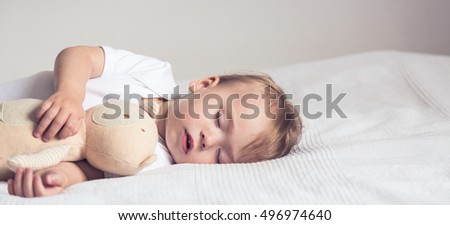Baby sleeping in crib. Peaceful baby lying on a bed while sleeping in a bright room with his teddy bear. Panoramic view.