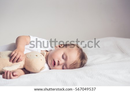 Sleeping baby in bed, holding a teddy bear.