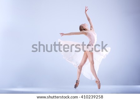 Young and incredibly beautiful ballerina is posing and dancing in a white studio full of light. The photo greatly reflects the incomparable beauty of a classical ballet art.