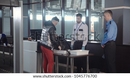 Officer throwing away forbidden things out of passenger cabin baggage standing at counter in airport.