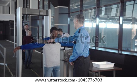 Multiracial people in airport going through gates having security control with guards.