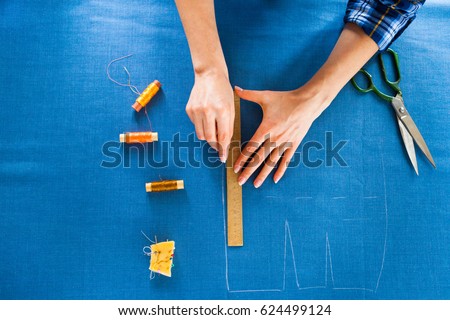 Close up. hands woman Tailor working cutting a roll of fabric on which she has marked out the pattern of the garment she is making with tailors chalk.