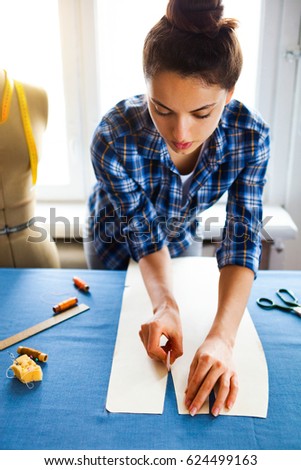 Close up. hands woman Tailor working cutting a roll of fabric on which she has marked out the pattern of the garment she is making with tailors chalk.