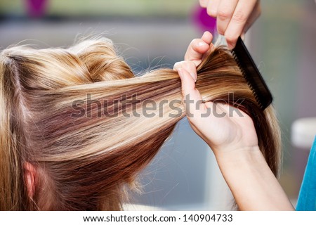 Closeup of hair dresser combing client's hair in salon