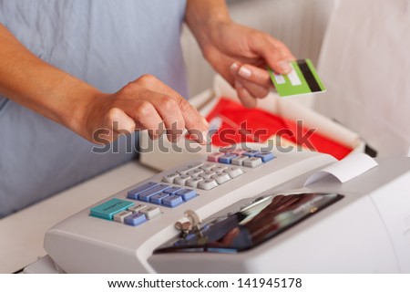 Midsection of saleswoman holding credit card while using ETR machine at boutique counter