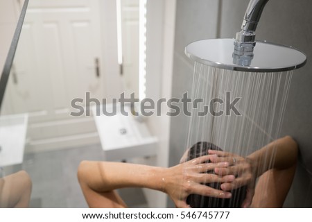 Person enjoying a communal shower in a large cubicle sitting under a large flat shower head letting the water run over their body, close up high angle view from behind