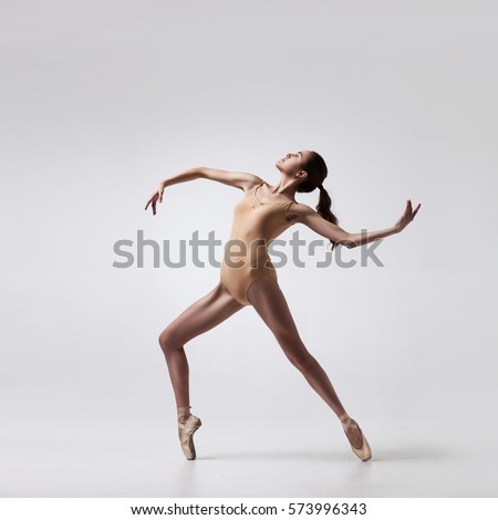 young beautiful ballet dancer in beige swimsuit posing on pointes on light grey studio background