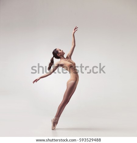 young beautiful ballet dancer in beige swimsuit posing on pointes on light grey studio background