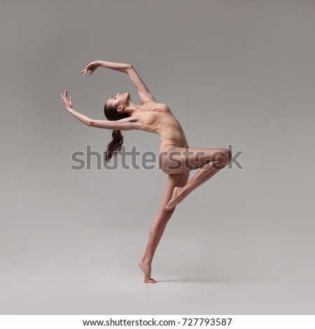 young beautiful ballet dancer in beige swimsuit posing on grey gradient studio background