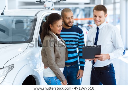 Filing document. Shot of a handsome salesman filing documents with his happy clients at the dealership