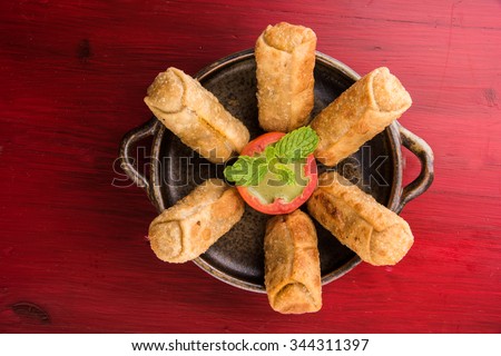 veg roll in brown ceramic bowl with mint leaf, isolated on red wooden background, top view