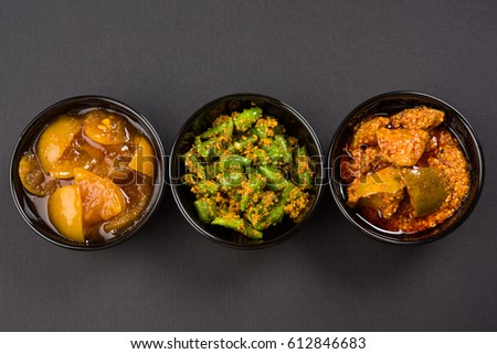 Group photograph of indian pickles like mango pickle , lemon pickle and green chilli pickle, sarved in black ceramic bowl, selective focus