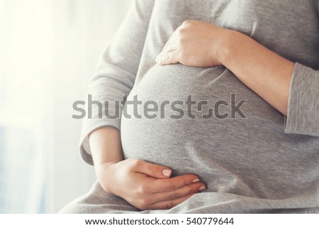 Young pregnant woman holds her hands on her swollen belly. Love concept. Horizontal with copy space