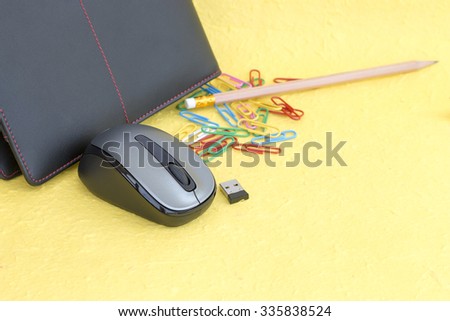 Wireless mouse with notebook and paper clip on yellow background