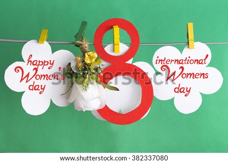 figure 8, paper flowers hang on clothespins in front of green background. International Women's Day. March 8, Happy Women's Day greeting message text