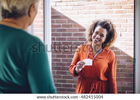 Healthcare worker showing her badge at the front door of a senior womans home.
