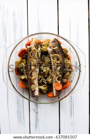 Baked roasted fried fish with baked, baked, gifted vegetables on a white wooden table