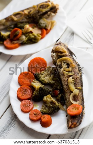Baked roasted fried fish with baked, baked, gifted vegetables on a white wooden table