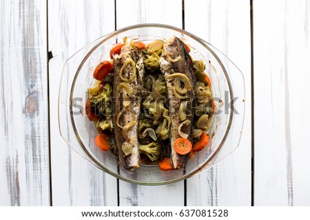 Baked roasted fried fish with baked, baked, gifted vegetables on a white wooden table
