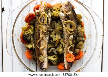 Baked roasted fried fish with baked, baked, gifted vegetables on a white wooden table