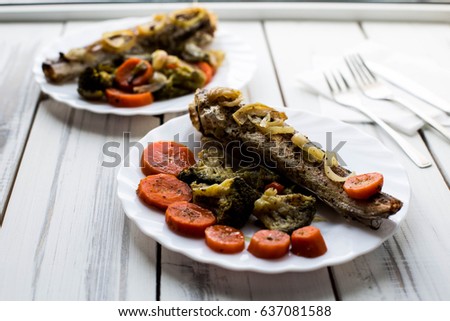 Baked roasted fried fish with baked, baked, gifted vegetables on a white wooden table