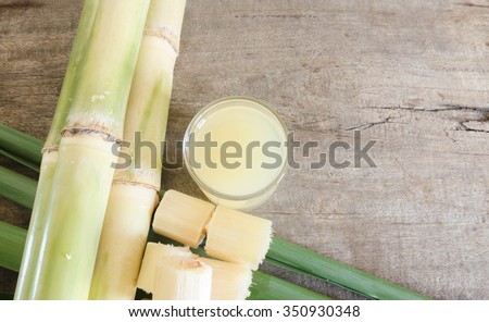 Freshly squeezed sugar cane juice in glass with cut pieces cane on a wooden table.