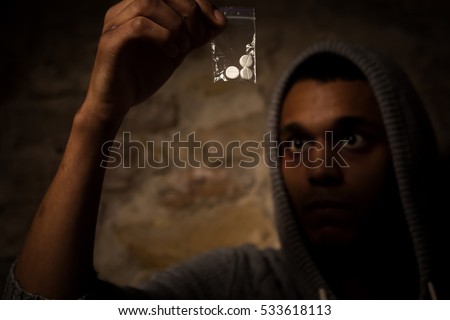 Drug addict man holding white powder in front of him. Man looking on drugs and showing it to camera.