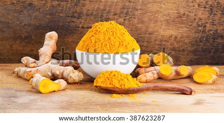 Turmeric roots with turmeric powder on wooden background