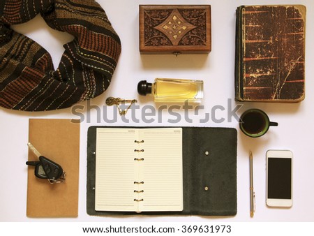 Men's or women's different accessories: brown scarf, golden brooch, perfume, white cellphone, empty notepad, pen, car keys, vintage book, wooden box on white background