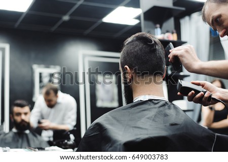 Master cuts hair and beard of men in the barbershop, hairdresser makes hairstyle for a young man