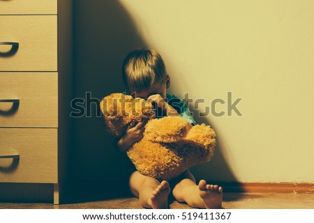 Lonely scared boy sitting in corner, hugging his teddy bear and crying. Child abuse