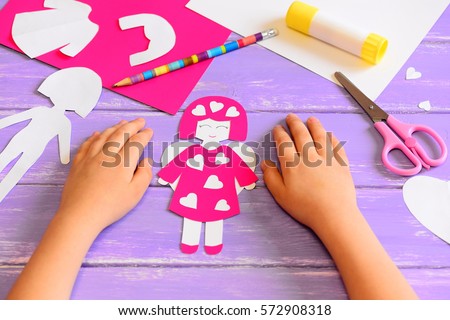 Child made an angel doll of cardboard. Childrens hands on a wooden table. Tools and materials for a fun kids art and craft activity. Valentine's day crafts idea for kids