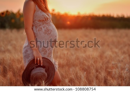 the pregnant girl with a hat in the field of wheat on a sunset