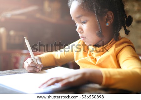 Profile of little African girl writing at home.