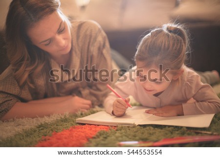 Beautiful blonde Caucasian girl lying on the floor with her mother and drawing.