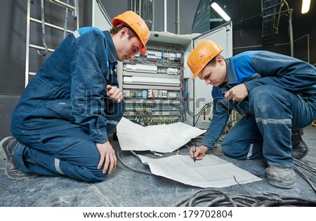 two electrician builder engineer with blue print scheme project in front of fuse switch box