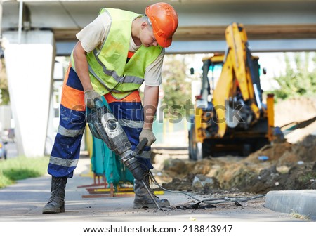 Builder worker with pneumatic hammer drill equipment breaking asphalt at road construction site