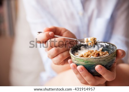 Young woman with muesli bowl. Girl eating breakfast cereals with nuts, pumpkin seeds, oats and yogurt in bowl. Girl holding homemade granola. Healthy snack or breakfast in the morning..