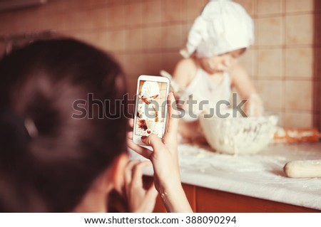 Mom takes photos with her phone like a little boy playing with a fry test on the table in an apron and chef's hat
