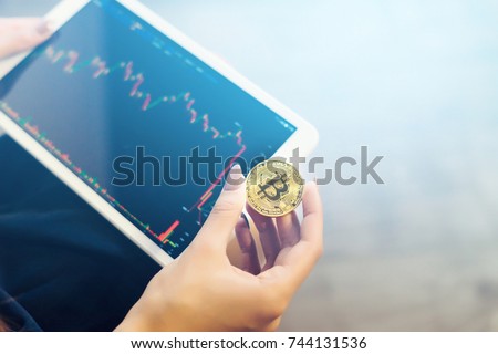 modern successful girl holds a gold bitcoin and a tablet with charts of crypto currency