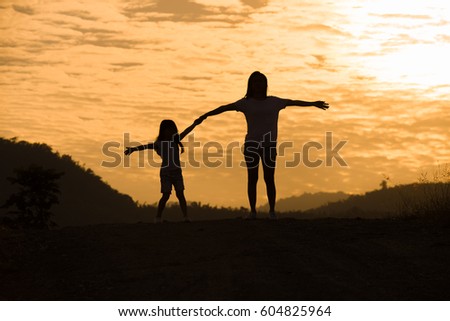 Mother encouraged Daughter outdoors at sunset, silhouette concept