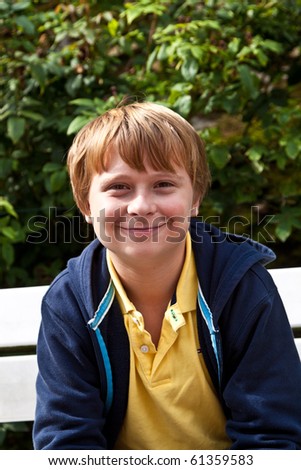 cute smiling young boy sitting on a bench in a garden