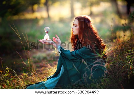 stock photo beautiful red haired girl in green medieval dress in glowing sun holding a sand glass and looking 530904499