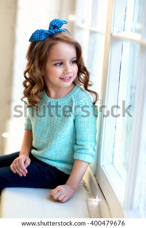 stock photo happy little girl with curly brown hair in a blue blouse with a barrette in her hair sitting on a 400479676
